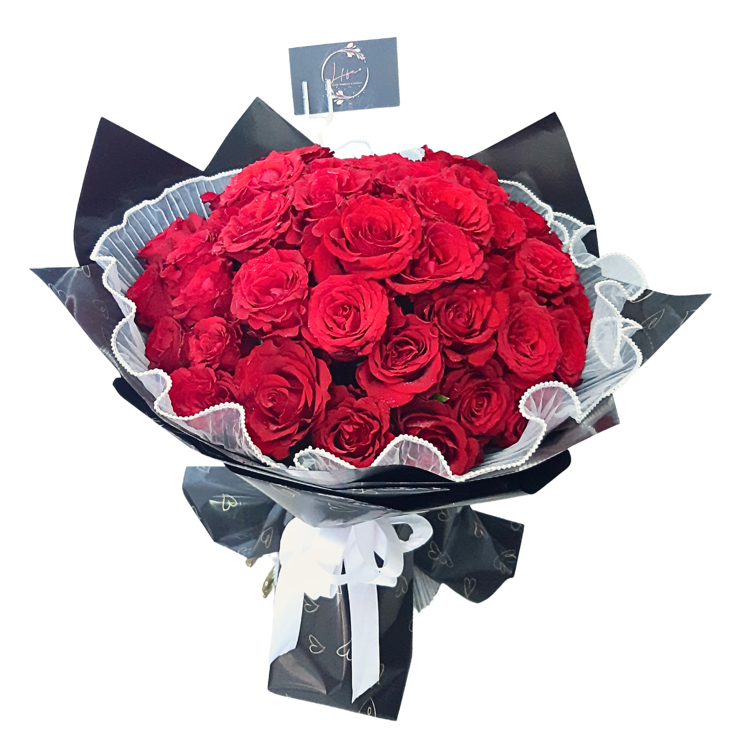 Bouquet of 50 red roses wrapped in black paper with hearts print and tied with white ribbon.
