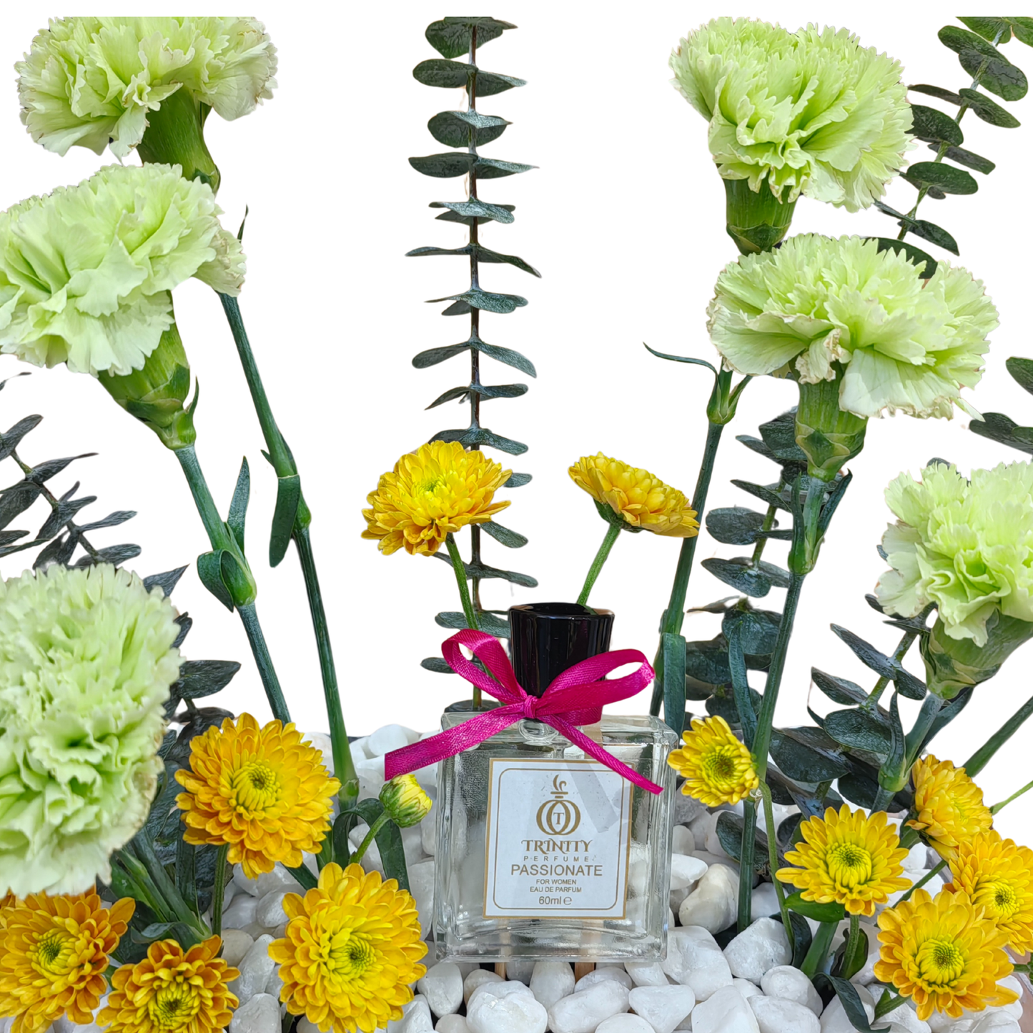 Perfume bottle with a pink ribbon surrounded by green and yellow flowers on white pebbles.