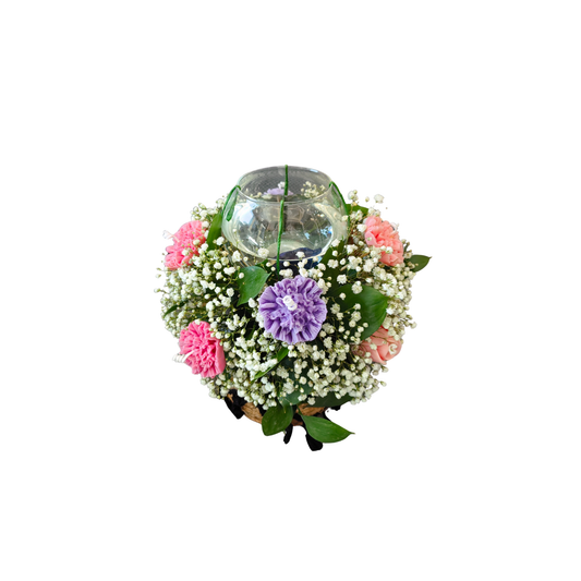 Decorative flower arrangement of pink and purple carnation flower candles, fresh white gypsophila and ruscus leaves around a clear glass candle holder.