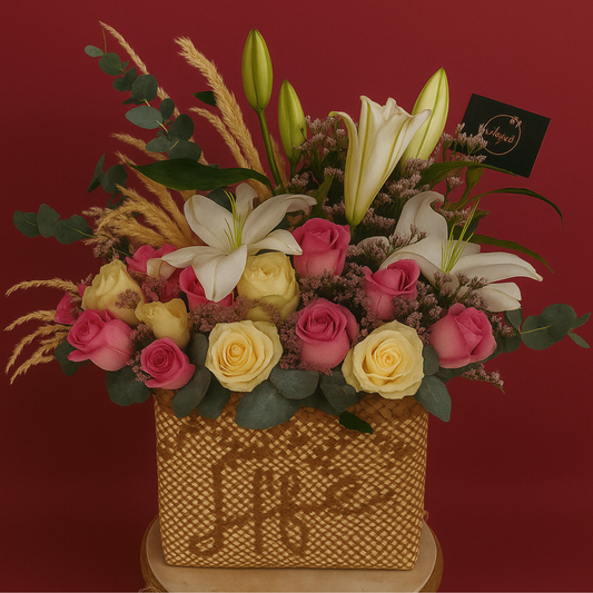 Ethereal Blush floral arrangement with pink and white roses, lilies, limoniums, eucalyptus, and pampas grass in a handwoven buri bag. Solid maroon background.
