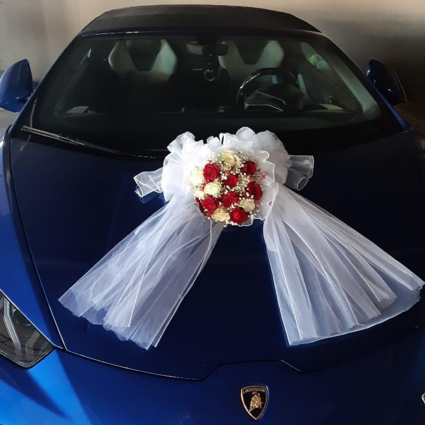 Sitting pretty, LOVE ABLAZE wedding car arrangement with red and white roses, on a blue Lamborghini car hood.